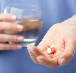 hand holding glass of water and medicines on the other